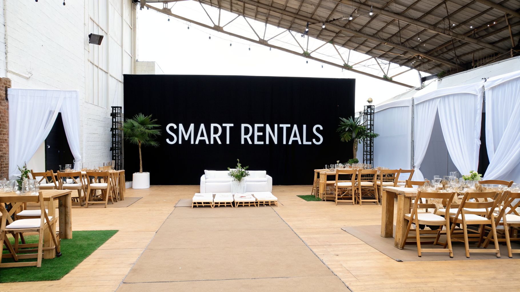Modern event venue with wooden tables, white chairs, lounge seating, and a large SMART RENTALS sign.
