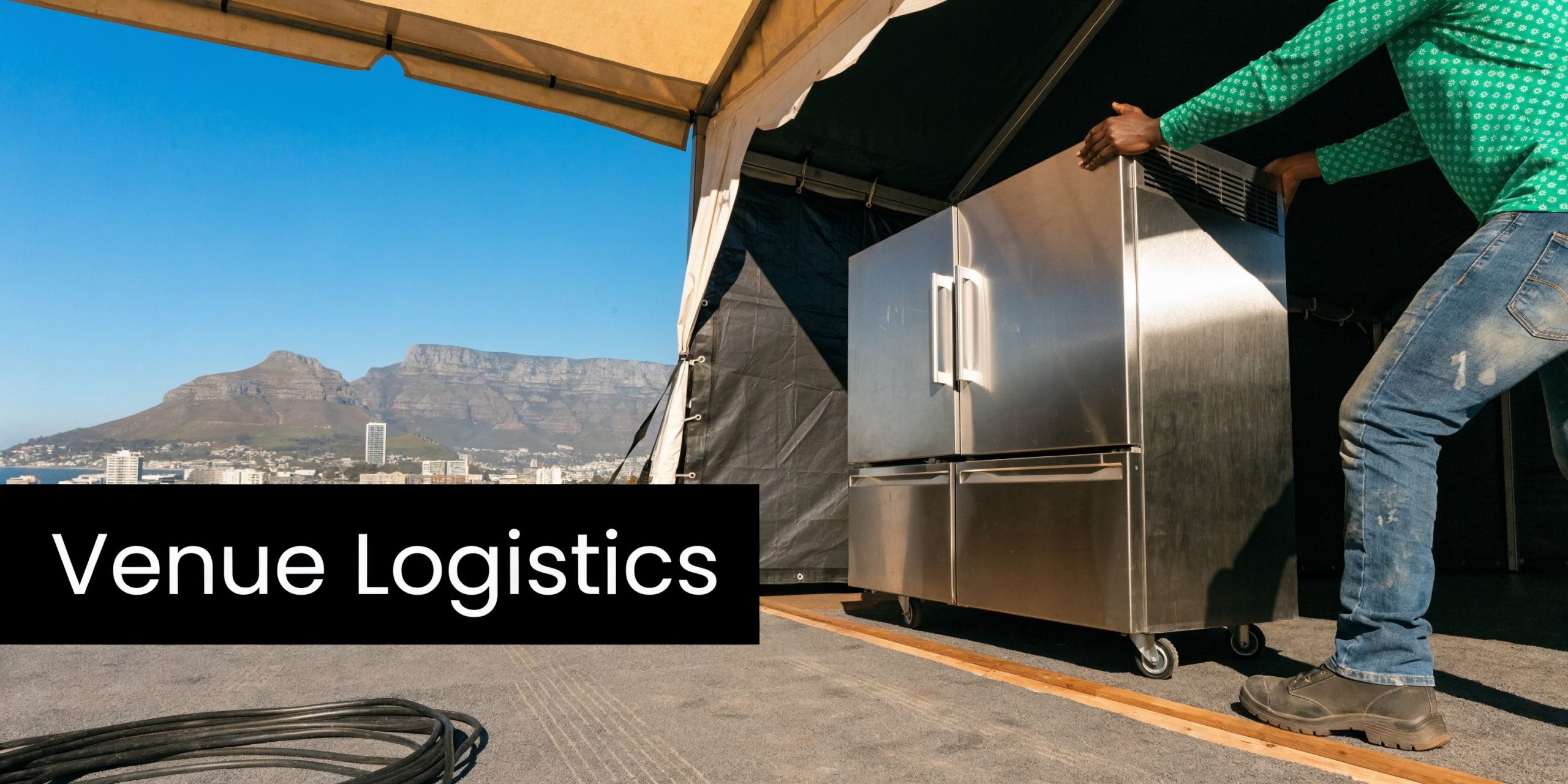 A worker in a green shirt moves a large stainless steel commercial freezer at a mountain event venue.