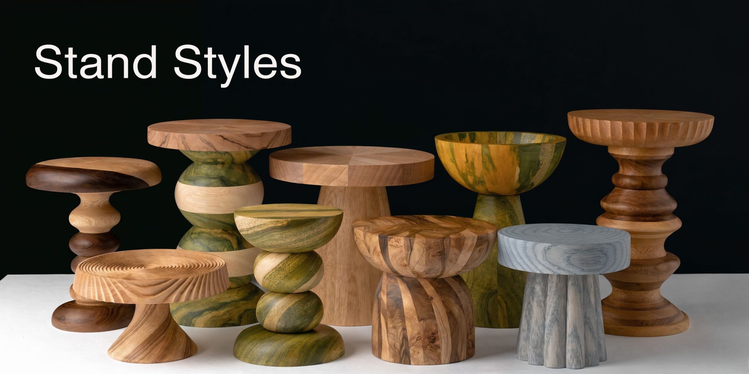 A collection of various artistic wooden cake stands arranged on a white surface against a black background.