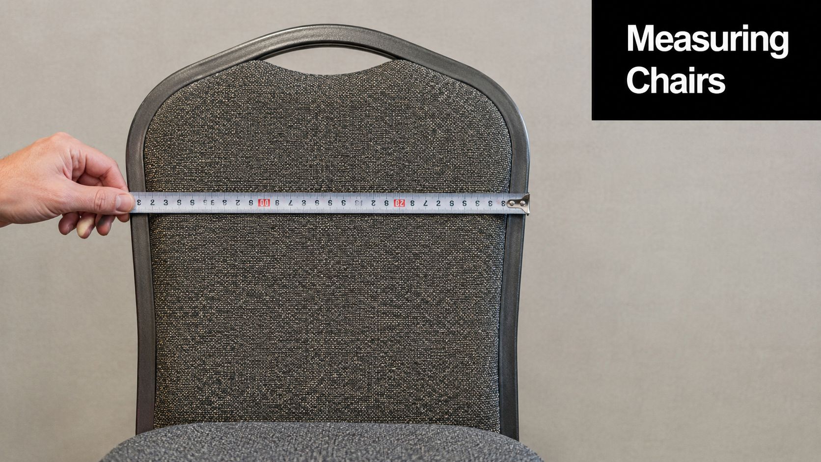 A person using a tape measure to check the width of a grey upholstered banquet chair back.