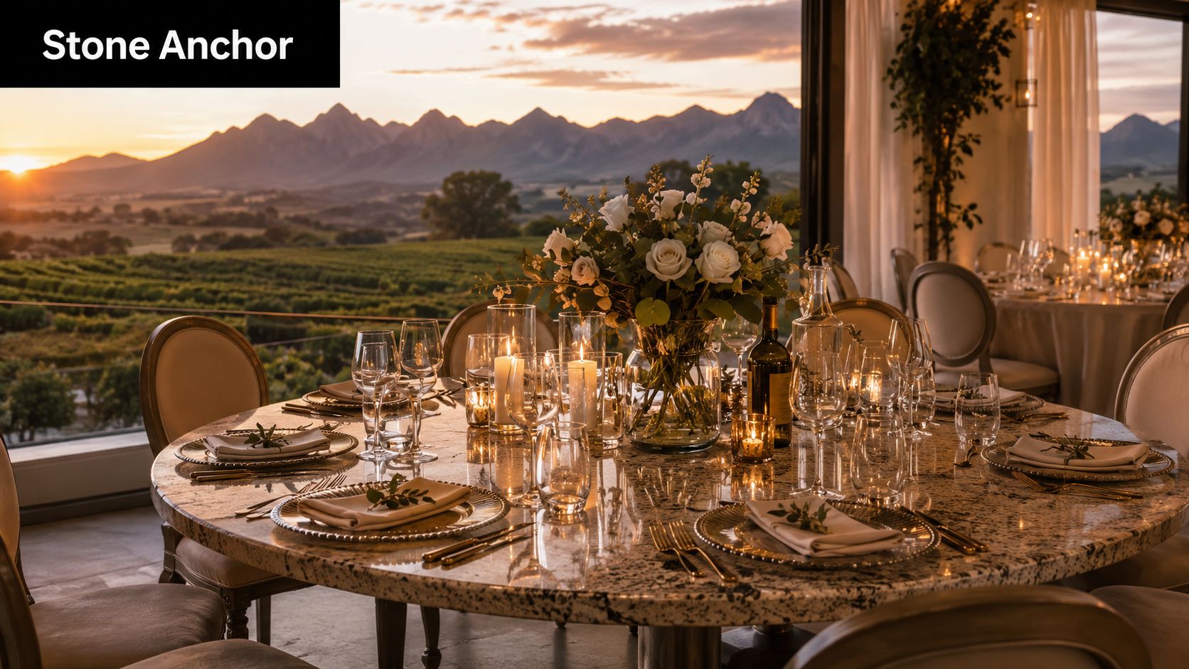 A luxurious round granite top table set for dinner with flowers, glasses, and a mountain vineyard view.