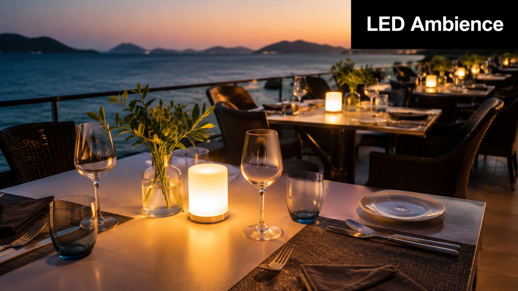 An elegant outdoor restaurant table setting with glowing LED lamps at sunset overlooking the calm ocean.